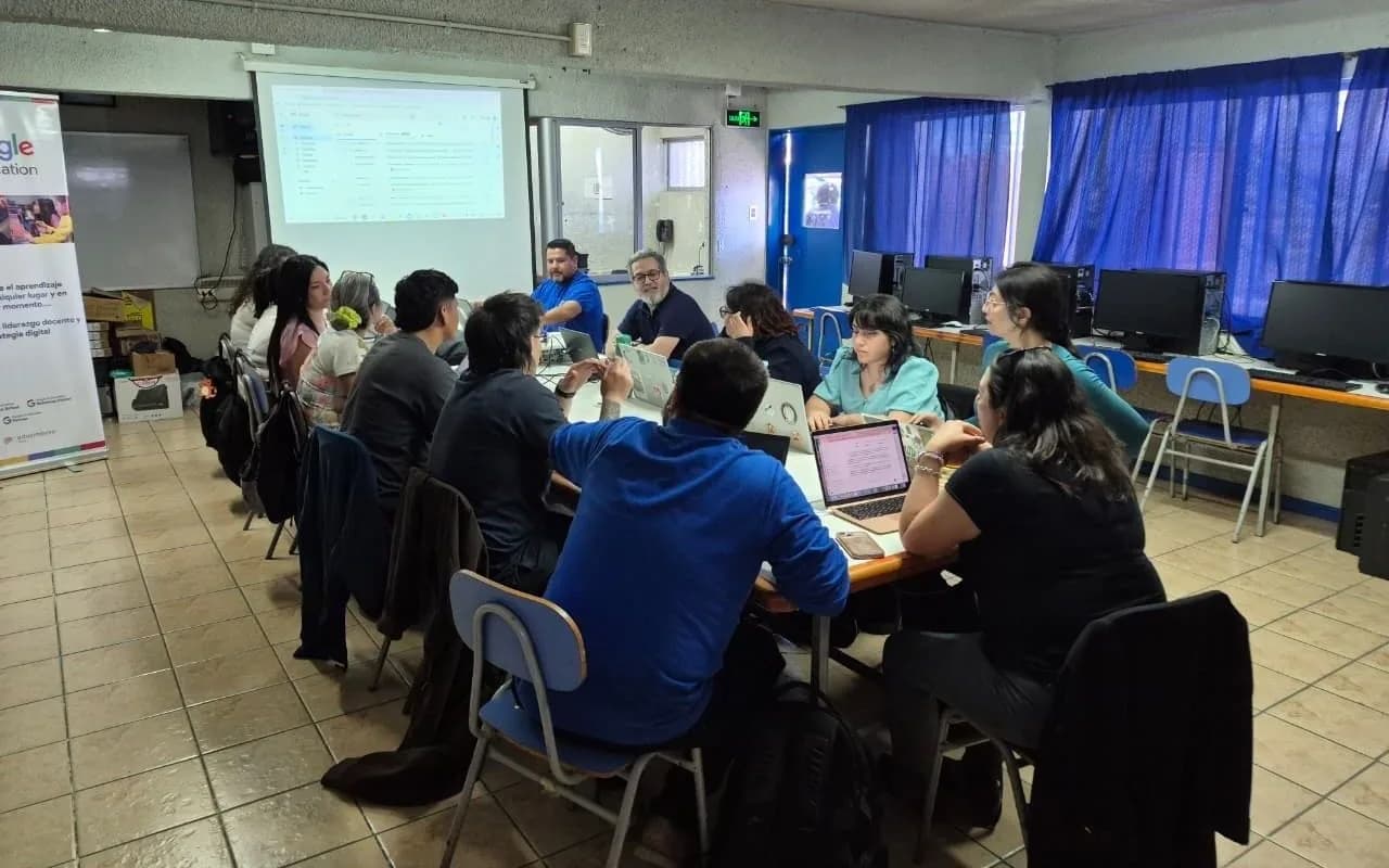 Docentes colaborando con sus portátiles en una sala de clases con cortinas azules.